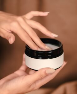 Hands lifting the lid from a white moisturizer jar