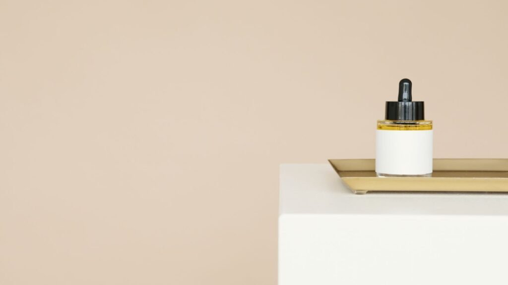 A glass dropper bottle of facial oil on a tray against a beige background